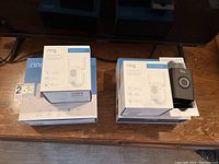 Photo showing Ring Chime Pro Wi-Fi extenders and one Ring Video Doorbell II on wooden surface with box packaging
