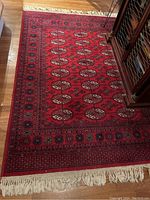 Full view of rectangular Persian style area rug in red with black and white patterns, showing fringed edge and some corner wear.