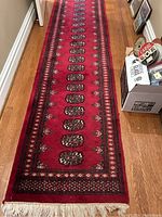 Full length of the red Persian style runner rug showing central geometric motifs and borders with fringed end.