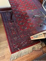 Photo showing the red Persian style rug with traditional medallion and border patterns, placed under office and living room furniture, showing fringe and some wear.