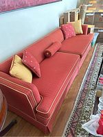 Red sofa with reversible cushions, yellow and red throw pillows on hardwood floor next to patterned rug and stacked boxes