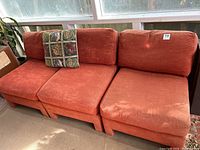 Front view of three rust orange modular sofa sections with loose cushions and decorative throw pillow