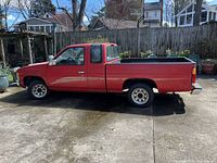 Left side profile of red Nissan pickup showing extended cab and bed liner