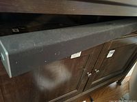Photo of black Vizio sound bar placed on dark wooden cabinet, showing fabric front and rectangular shape with slightly rounded edges.