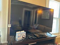 55 inch Vizio television placed on wooden stand with antenna box and Blu-ray player on stand, photo shows TV front and other devices.