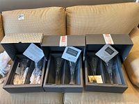 Three grey presentation boxes opened on beige couch, each containing two crystal champagne flutes with paperwork.