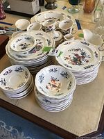 Photo showing stacked plates, bowls, cups, and saucers with floral and botanical pattern on white china.