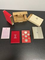 Full set packaging and all contents laid out: red display case containing proof coins, protective box components, information pamphlet, and outer sleeve.