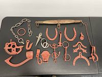 Display of metal antique farm equipment parts on black surface including horseshoes, hooks, chain, gear piece, and wooden handled yoke component.