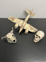 Three aquarium decorations on a table: an airplane, a human skull, and a horned skull.
