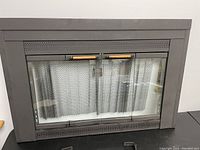 Front view of the refurbished fireplace door and screen with closed double glass doors, metal mesh screen visible inside, and wood handle accents.