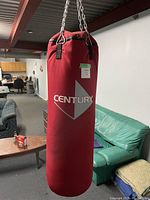 Full view of a red Century punching bag hanging from chains indoors, showing logo and condition