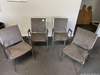 Full view of four stacking chairs arranged together showing grey cloth seats and backs, metal frames, and wood armrests.