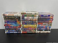 31 VHS tapes arranged in three stacks showing titles like Jumanji, Oliver!, Bambi, Sleeping Beauty, Matilda, Beauty and the Beast, Cinderella, ET.