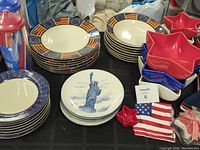 Shows dinner plates with American flag design around the rim, red star-shaped bowls, blue and white plates with Statue of Liberty design, small flag and themed items.