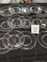 Top view of all 14 clear glass plates showing the distinctive raised bead border pattern of the Candlewick design, arranged in overlapping pattern on dark tablecloth.