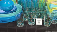 Photo showing large tumblers, rocks glasses with occasional blue and green dots, stacked blue bowls, and three beach towels.