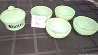 Set of four pale green FireKing jadeite cereal bowls and one covered butter dish with lid on dark cloth.