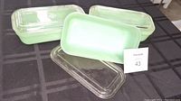 Set of three FireKing jadeite glass loaf pans with clear lids shown on a black tablecloth.