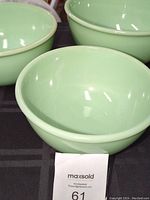 Set of three nested jadeite green mixing bowls displayed on black cloth, visible bowls are round with even smooth edges and glossy surfaces.