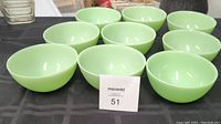Twelve light green jadeite bowls arranged in three rows on a black surface.