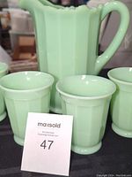 Front view of the pitcher with four cups around it, all in light green jadeite glass.