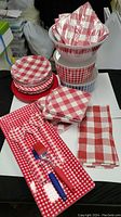 View of melamine and paper plates, paper napkins, rectangular trays with gingham pattern, and serving spoons with blue handles.