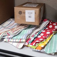 Photo showing folded cotton dish towels stacked together and a brown box on top with a MaxSold label.