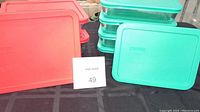 Photo shows red and teal plastic lids on Pyrex glass storage containers arranged on table, highlighting lid colors and batch quantity