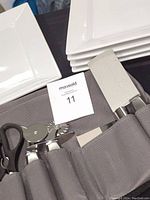 Photo showing stacked white ceramic square servers, part of Wolfgang Puck kitchen accessory roll with scissors, pizza cutter, and peelers visible.