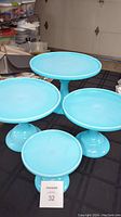 Four blue cake stands displayed on a dark surface, showing size gradation and pedestal bases.