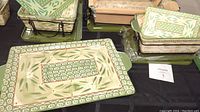 Overview of three rectangular ceramic casseroles with Old World Green pattern, placed in wrought iron holders. Some lids and trivets visible.