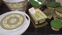 Overview of multiple bakeware and serveware items including round melamine plates, various sizes of covered bowls and casseroles with lids and wrought holders, and a large beverage tub, all in Old World Green pattern.