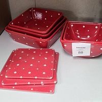 Photo showing 3 red nested square baking dishes with white polka dots, 3 matching red bowls, and 3 red glass cutting boards with polka dots.