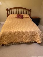 Full view of the made bed showing wooden spindle headboard, beige quilted cover, striped dust ruffle, and small decorative pillow