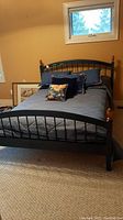 Full view of assembled double bed with grey bedding, decorative pillows, metal frame with wooden finials on head and foot boards