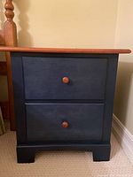 Front view of two-drawer bedside table, navy blue body with natural wood knobs