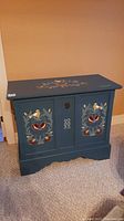 Front view of blue wooden chest with colorful floral hand-painted designs on front panels and top, showing the lid and lock.