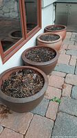Five round clay flower pots arranged in a line near a window, filled with soil and debris.