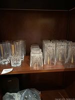 Photo showing all crystal glasses arranged on a wooden shelf, including both smaller and taller glasses with cut crystal patterns.