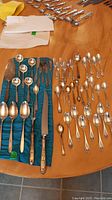 Full view of assortment of 37 spoons, forks, and serving utensils arranged on table and cloth