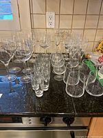 Photo showing wide selection of drinking glasses arranged on counter including wine, brandy, liqueur, champagne, and water glasses.
