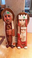 Front view of two carved festive wooden floor figures showing a man with a key and a crowned adult with a child.