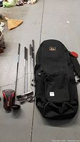 Overview of all left-handed golf clubs and black travel bag on concrete floor