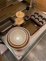Overview of ceramic mixing bowls stacked, metal loaf pan, muffin tin, rectangular baking pan, juicer and bottle.