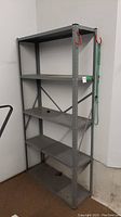 Front view of the metal shelving unit showing five shelves, red hooks on top corners, and green rope hanging on the side.