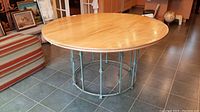 Full view of round wooden table with smooth top and round iron base structure on tile floor.