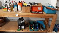Overview of tools on wooden shelf including battery charger, boxed socket set, Black & Decker drill, and containers with nails and screws.