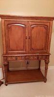 Front view of wooden TV cabinet showing two doors with carved trim, two drawers, and lower open shelf.