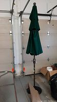 Full view of folded green patio umbrella with attached brown two-section pole standing upright indoors.